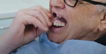 An old american man inserts a denture in his mouth